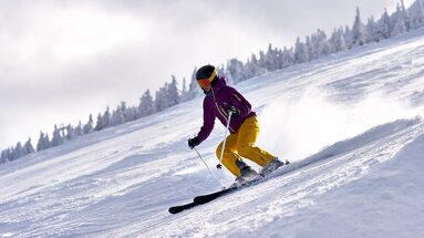 Eine Frau in gelb-lila Skikleidung fährt eine Abfahrt am Großen Arber auf ihren Skiern hinuter. | © Bodenmais Tourismus & Marketing GmbH